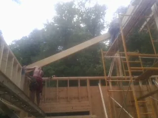 Carpenter raising a rafter beam on a new second story frame in Norris