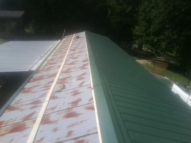 Old rusted panels beside newly installed green metal roofing — Wind Damage Roof Repair by Roofing Brothers in Norris
