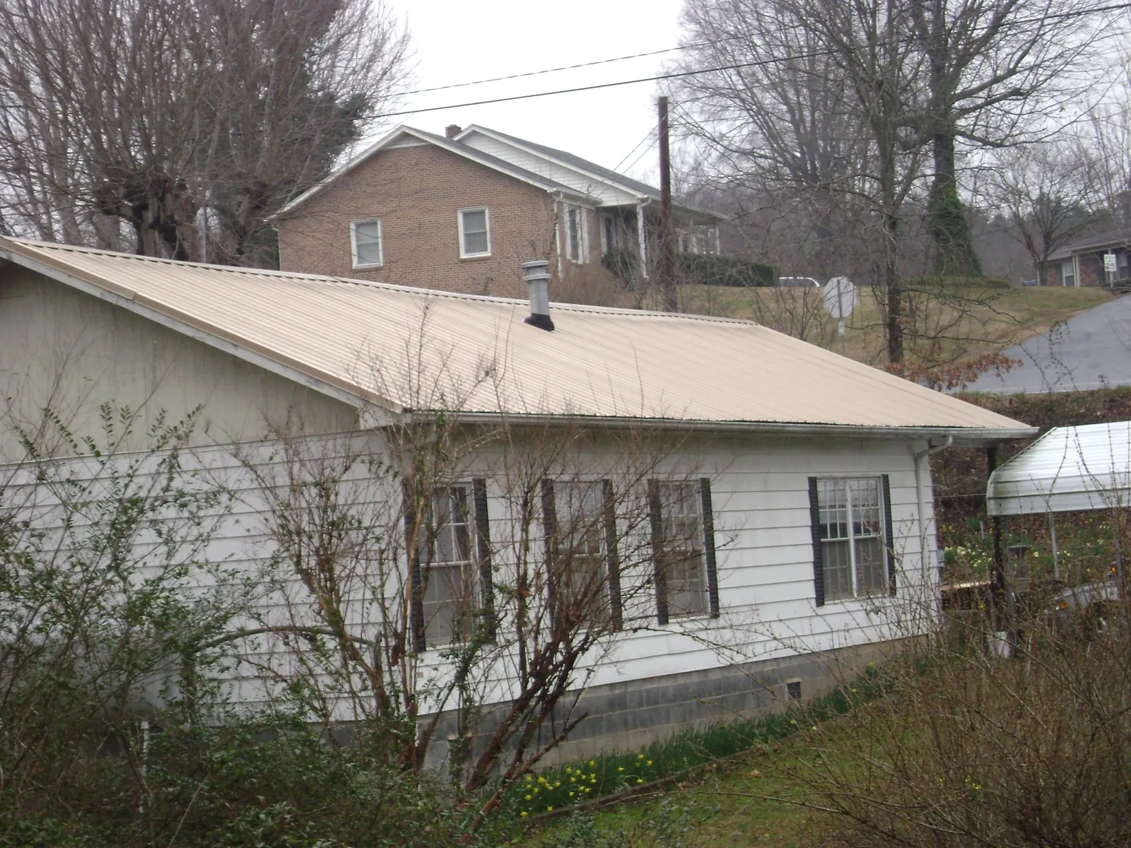 Tan metal roof on a white sided house set into a hillside — Commercial Roofing by Roofing Brothers in Norris