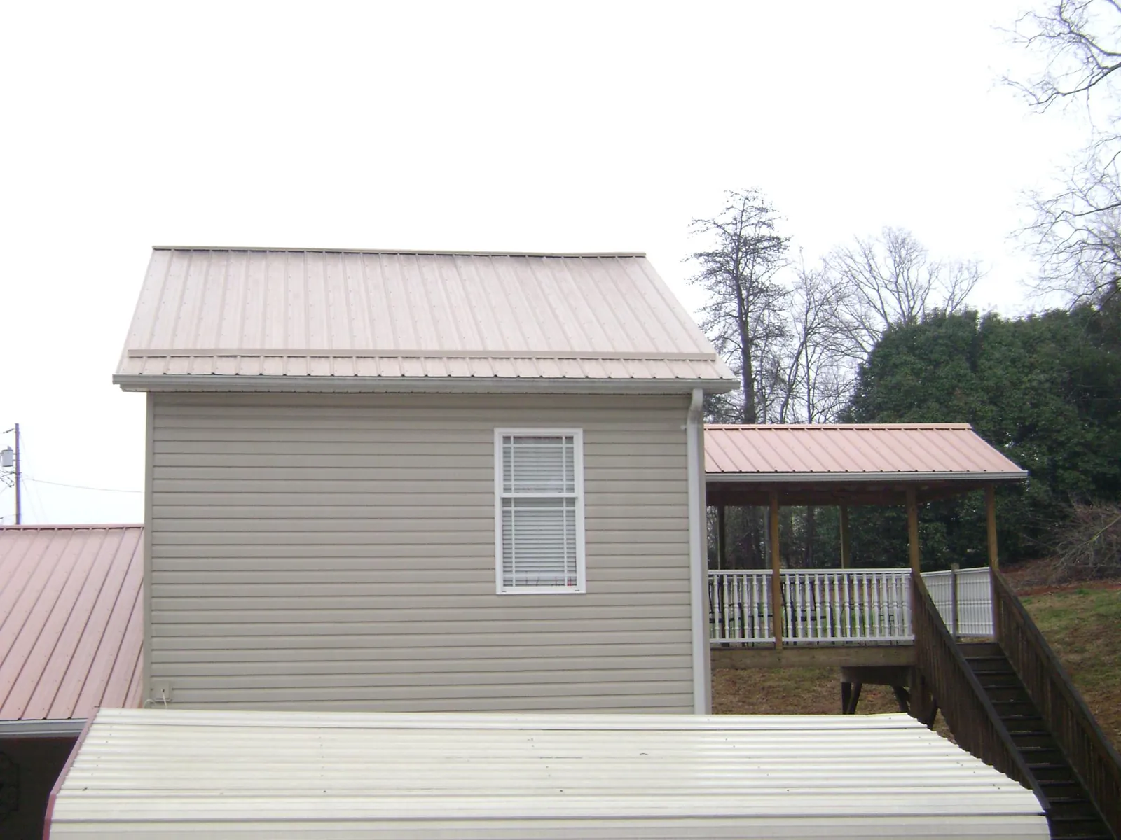 Tan metal roofs on a two story addition and attached porch, from a Roof Replacement job in Norris